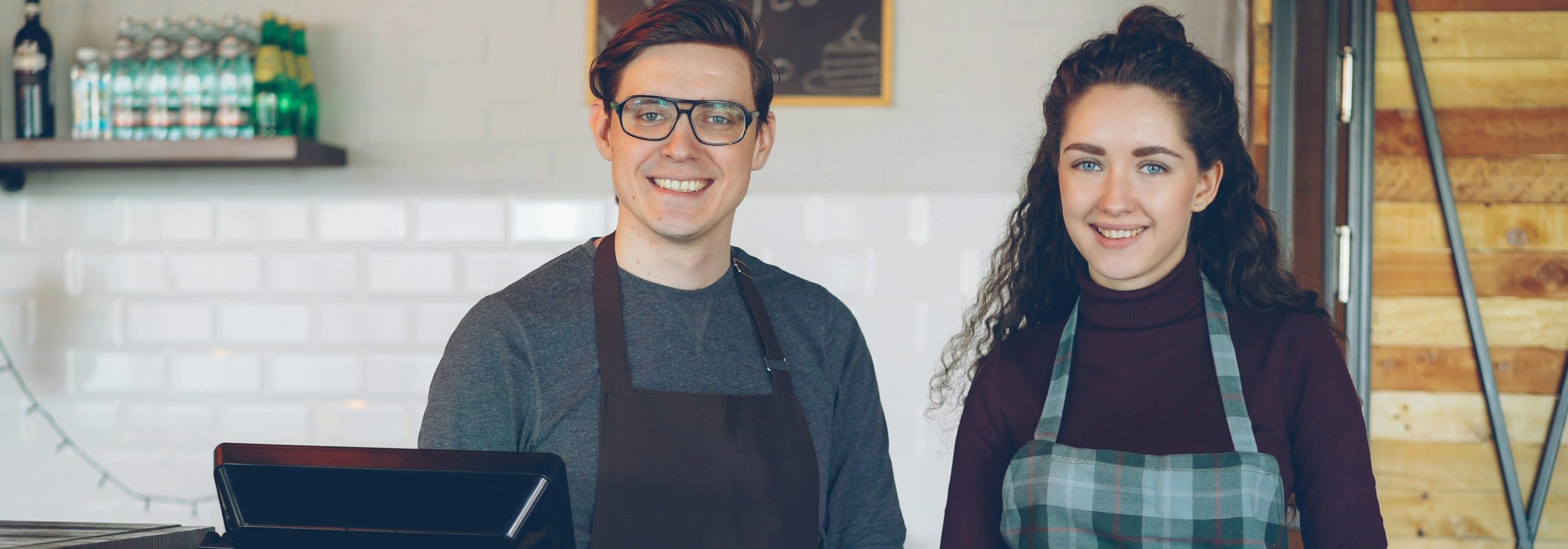 Two small business owners smiling behind the counter of their café