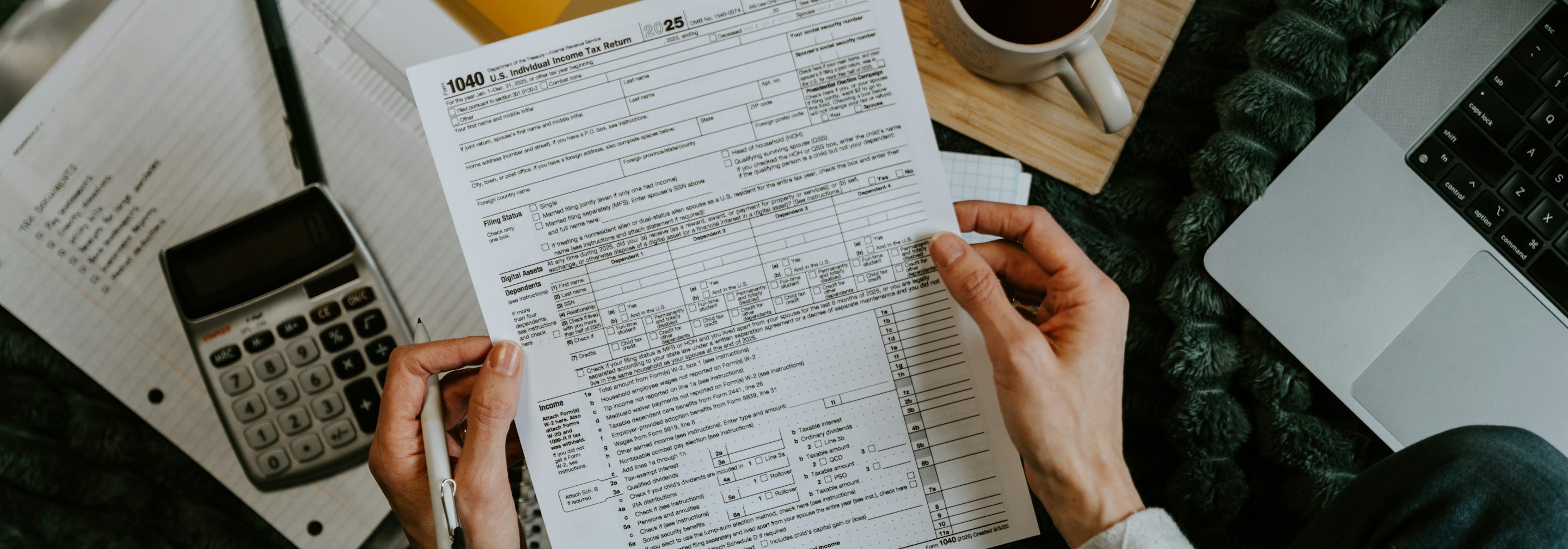 Hands holding a Form 1040 beside a calculator and laptop