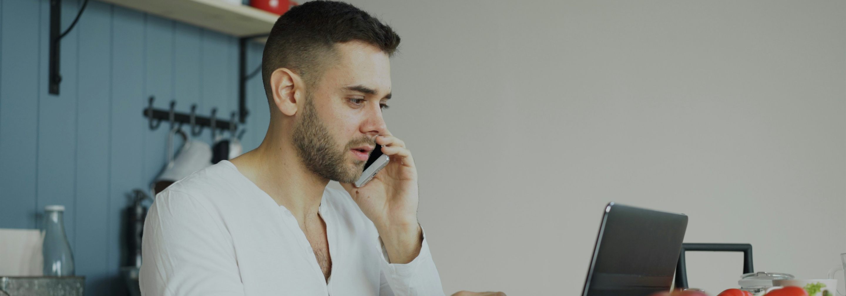 A man at his kitchen table, on the phone while working through his taxes on a laptop