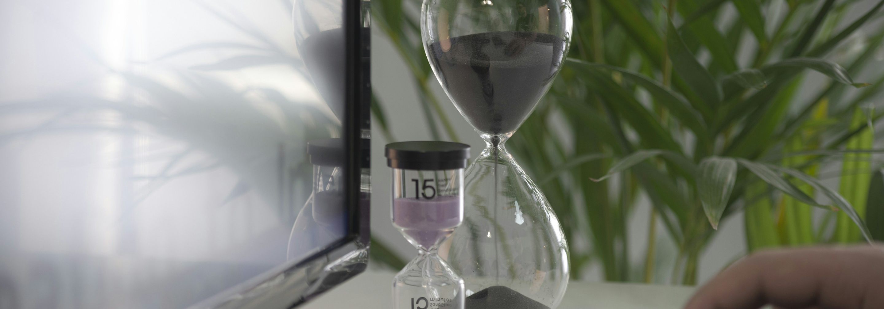 An hourglass on a desk beside a laptop