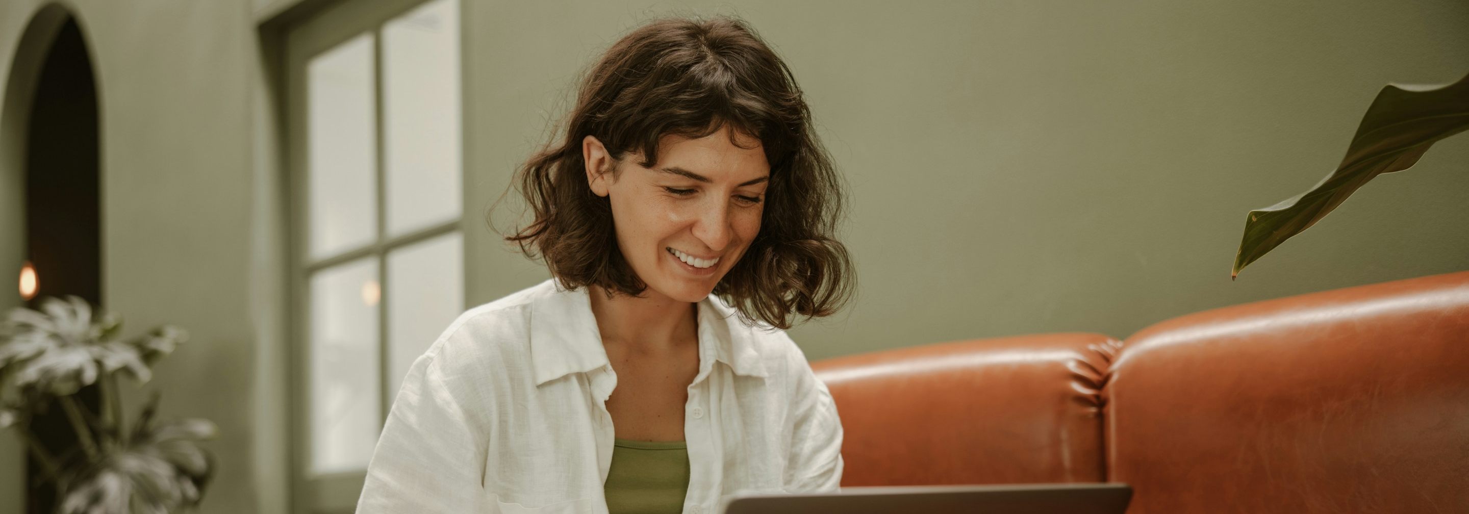 A woman smiling as she files her taxes on a laptop from her sofa